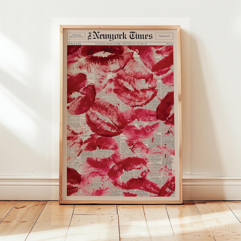 Pu&ograve; includere: Una stampa incorniciata con un collage di segni di baci di rossetto rosso su uno sfondo di giornale vintage. Il giornale &egrave; del New York Times, datato luned&igrave; 21 giugno. La stampa &egrave; esposta su un pavimento in legno.