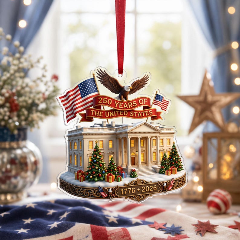 May include: A festive ornament depicting the White House, American flags, and an eagle. The ornament commemorates "250 YEARS OF THE UNITED STATES" with the years "1776 * 2026". It includes Christmas trees and gift boxes, suitable for the holiday season.