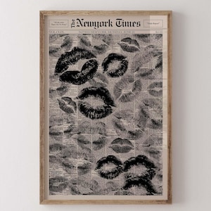 Puede incluir: Impresi&oacute;n enmarcada con un collage de marcas de besos de l&aacute;piz labial negro sobre un fondo de peri&oacute;dico vintage. El peri&oacute;dico est&aacute; fechado el 21 de junio, con el titular "The Newyork Times". La impresi&oacute;n est&aacute; en un marco de madera.