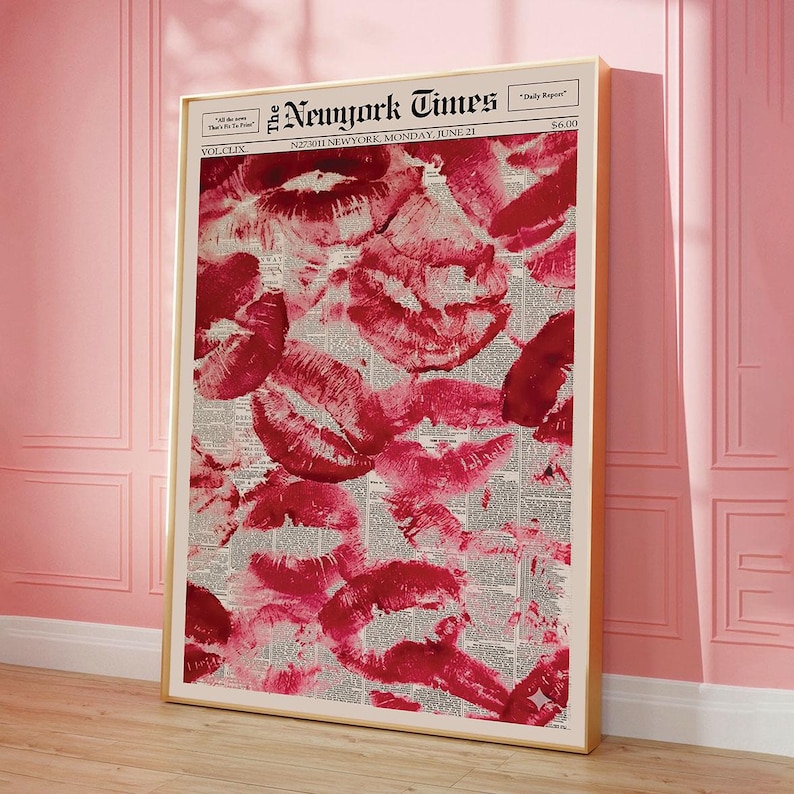 Pu&ograve; includere: Una stampa incorniciata con un collage di segni di baci di rossetto rosso su uno sfondo di giornale. Il giornale &egrave; il New York Times, datato luned&igrave; 21 giugno. La stampa &egrave; in una cornice dorata e appoggiata a un muro rosa.
