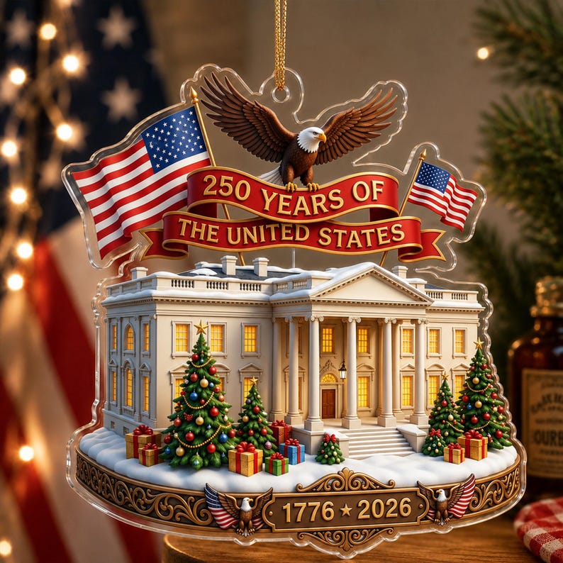 May include: A clear acrylic Christmas ornament depicting the White House, American flags, and a bald eagle. The ornament reads "250 Years of The United States" and "1776-2026". Decorated Christmas trees and gifts are in front of the White House.