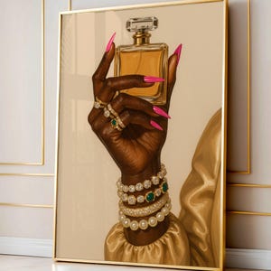 May include: A framed print depicting a dark hand holding a perfume bottle. The hand is decorated with rings, bracelets, and long pink nails. The perfume bottle is rectangular with a clear top and gold details. The background is a neutral beige colour.
