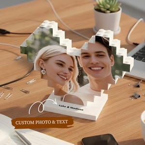 May include: A white, heart-shaped photo display made of interlocking blocks, featuring two smiling people. The base has the names "Luke & Madison" and the text "CUSTOM PHOTO & TEXT".