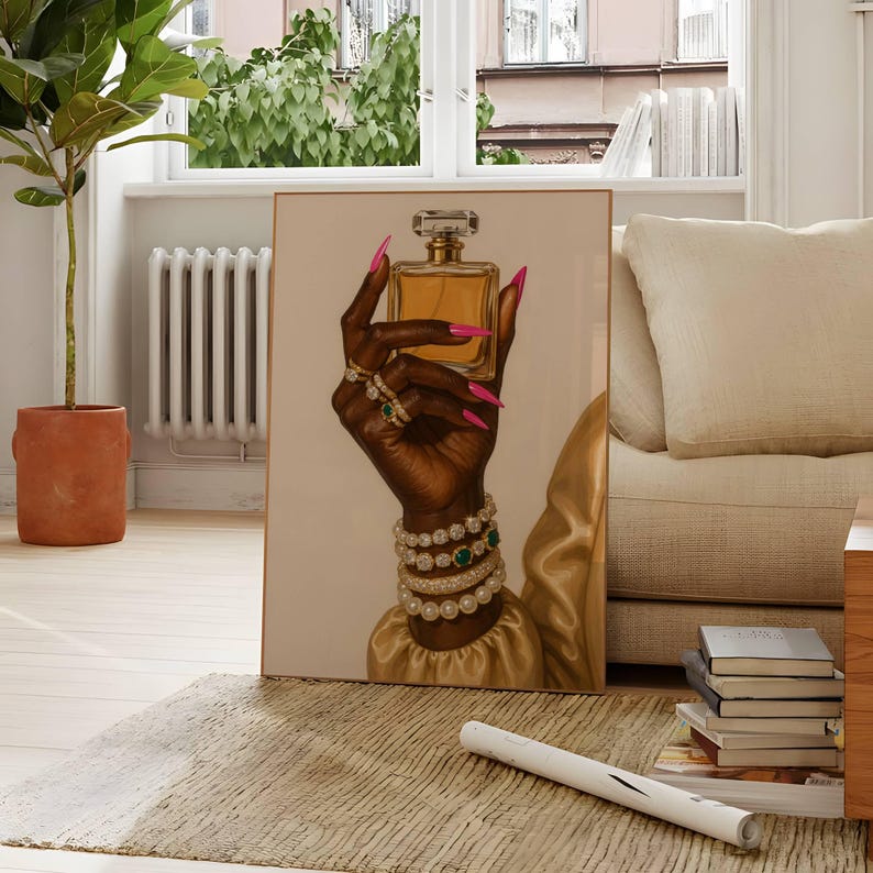 May include: An art print showing a dark hand holding a gold perfume bottle. The hand is decorated with rings, bracelets, and long pink nails. The artwork is set against a neutral background, with a gold sleeve visible.