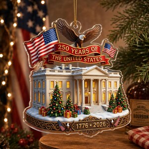 May include: A clear acrylic Christmas ornament depicting the White House, American flags, and an eagle. The ornament celebrates "250 Years of The United States" with the years "1776 * 2026". Presents and Christmas trees decorate the scene.