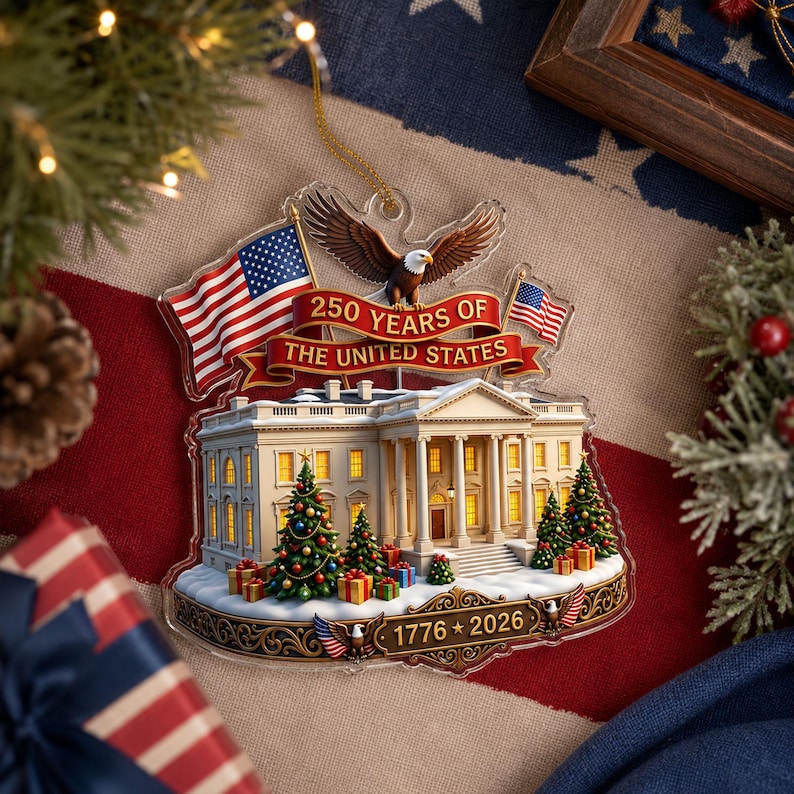 May include: A clear acrylic Christmas ornament depicting the White House, American flags, and an eagle. The ornament reads "250 Years of The United States" and "1776 * 2026". Decorated with Christmas trees and presents, it is a patriotic holiday decoration.