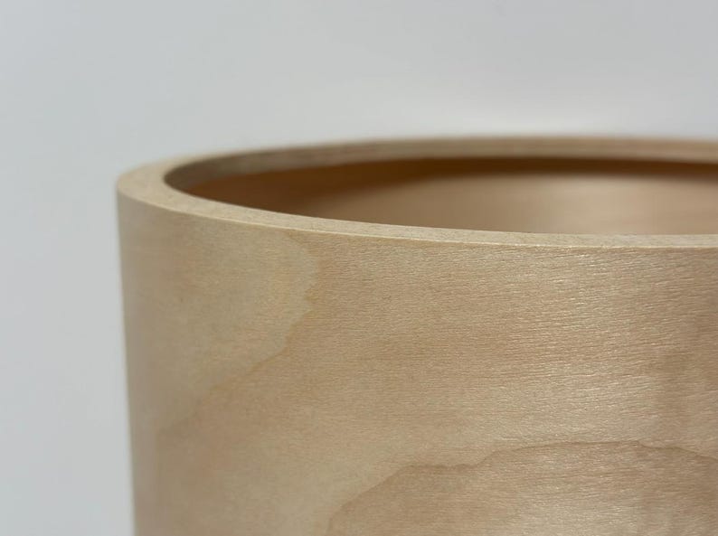 May include: Close-up of a light-colored wooden container. The cylindrical shape has a smooth, natural wood grain texture. The rim is rounded, and the interior is visible, suggesting a vessel for storage or display.
