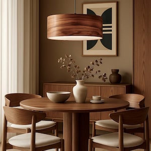 May include: A modern dining room set featuring a round wooden table and four matching chairs with cream-colored seats. A wooden pendant light hangs above the table. A vase with branches and a bowl are on the table.