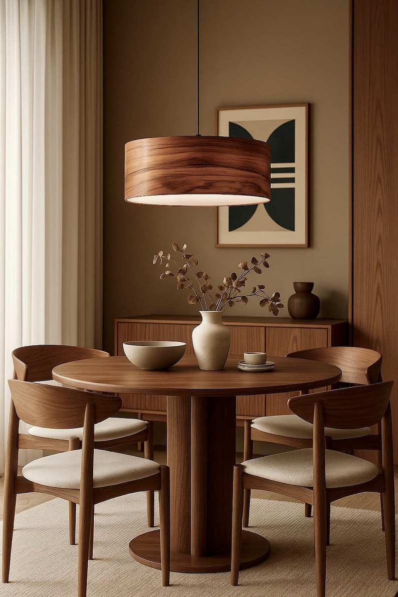 May include: A modern dining room set featuring a round wooden table and four matching chairs with cream-colored seats. A wooden pendant light hangs above the table. A vase with branches and a bowl are on the table.