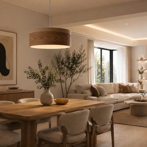 May include: A cylindrical wooden pendant light fixture hangs above a rectangular wooden dining table. The table is surrounded by four upholstered chairs and features a ceramic vase with green foliage and a small yellow bowl on its surface.