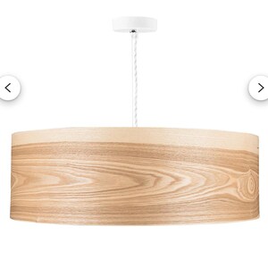 May include: A cylindrical pendant light fixture featuring a light-toned wood veneer shade with a visible natural grain pattern. The drum-shaped shade is suspended by a white cord connected to a matching white circular ceiling canopy mount.