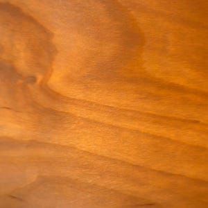 May include: Close-up of a wooden surface with a warm, amber hue. The wood grain is visible, creating a natural pattern of light and shadow. The texture appears smooth with subtle variations in tone.