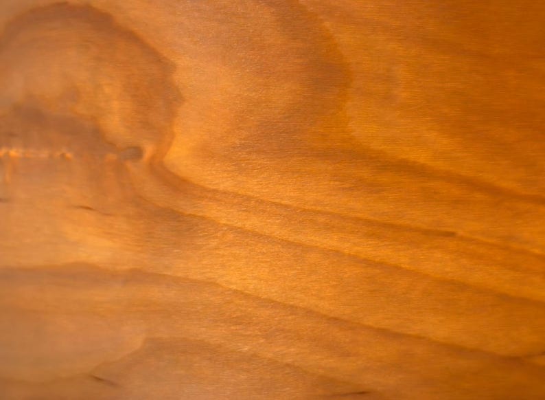 May include: Close-up of a wooden surface with a warm, amber hue. The wood grain is visible, creating a natural pattern of light and shadow. The texture appears smooth with subtle variations in tone.