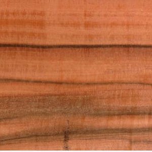 May include: Close-up of a piece of wood with a reddish-brown hue. The wood grain features dark, wavy lines that run horizontally across the surface. The texture appears smooth, with visible variations in color and pattern.