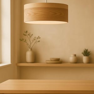 May include: A cylindrical pendant light fixture with a light-toned wood grain finish. The lamp features a smooth, circular frame suspended by a thin metal rod, providing a downward-facing light source with a clean, uniform appearance.