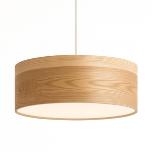 May include: A cylindrical pendant light fixture featuring a light-toned wood grain exterior finish. The drum-shaped shade is suspended by a single thin white cord and includes a flat, circular white diffuser panel at the bottom to soften light.