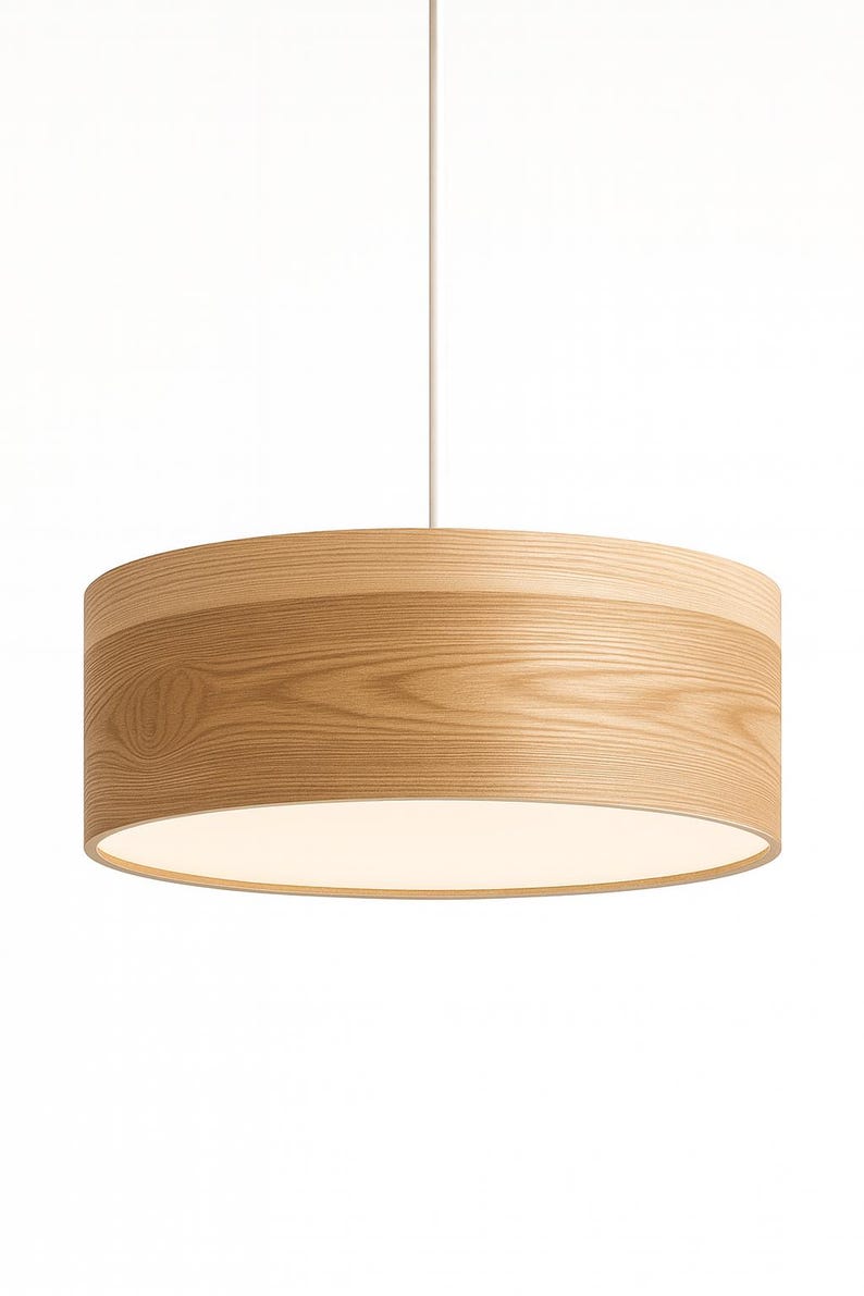 May include: A cylindrical pendant light fixture featuring a light-toned wood grain exterior finish. The drum-shaped shade is suspended by a single thin white cord and includes a flat, circular white diffuser panel at the bottom to soften light.