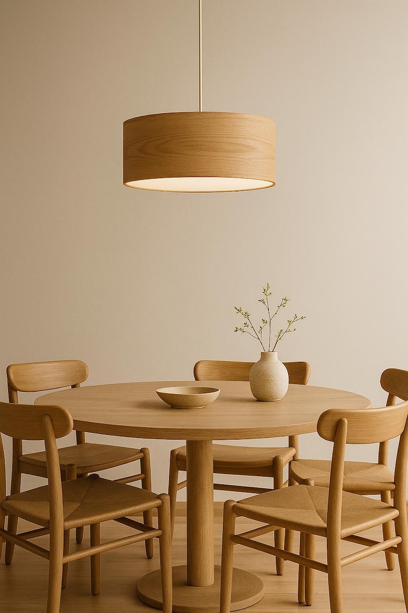May include: A dining room set featuring a round wooden table and matching chairs. A wooden pendant light hangs above the table. A vase with greenery and a bowl are on the table. The chairs have woven seats.