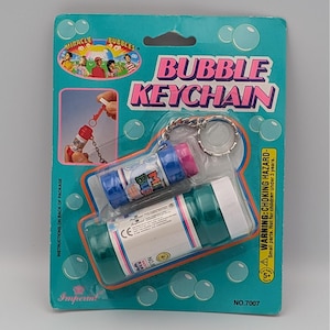 May include: A teal bubble keychain package with two bubble bottles. The package has the words "BUBBLE KEYCHAIN" in pink and white. The package also has the words "MIRACLE BUBBLES" and a warning about choking hazards.