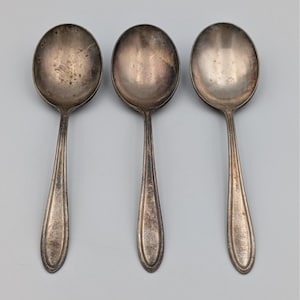 Puede incluir: Tres cucharas de plata antiguas con cuencos ovalados y mangos largos y delgados. Las cucharas muestran signos de edad y uso, con algo de deslustre en la superficie. Los mangos tienen un diseño simple y elegante.