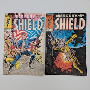 May include: Two vintage Marvel comic books featuring Nick Fury, Agent of S.H.I.E.L.D. Issue #1 shows a patriotic theme with an American flag background. Issue #2 depicts a space scene with a figure in a yellow spacesuit. Both comics have the number 200.