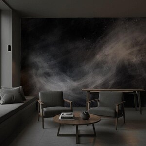 May include: A modern living room with dark gray walls and flooring. Two gray armchairs face a round wooden coffee table. A dark abstract mural covers the back wall. A wooden side table and a built-in bench with a pillow are also present.