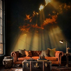 May include: A living room scene featuring a brown leather Chesterfield sofa with decorative pillows. A dark wooden trunk serves as a coffee table. The background is a mural of a dramatic sky with sun rays.