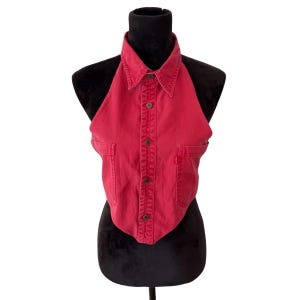 May include: A red denim halter top with a collared neckline and button-down front. The top features two small front pockets and is displayed on a black mannequin. The fabric appears to be a medium weight denim.