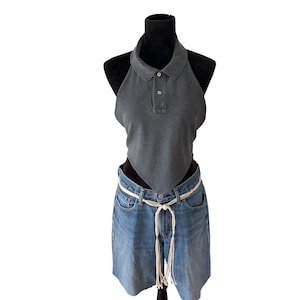 May include: A dark gray sleeveless halter top featuring a polo-style collar with a two-button placket, paired with light blue denim shorts that include a thin, white rope-style belt tied in a knot at the front with long, dangling ends.