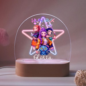 May include: A decorative night light with an anime-style illustration of three figures and a blue cat. The design is set against a pink star and the name "Gloria" is written below. The base is made of wood.