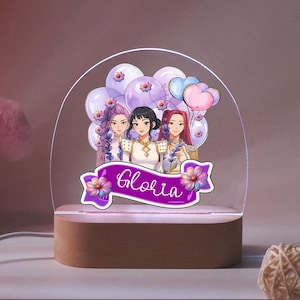 Op de afbeelding: Decoratieve LED-nachtlamp met een cartoonillustratie van drie vrouwen, ballonnen en bloemen. De naam "Gloria" staat op een paarse banner. De basis is van hout.