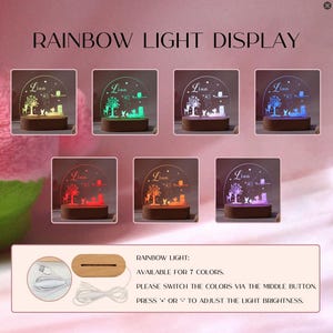 Op de afbeelding: Een regenbooglichtdisplay met zeven kleuropties. Elke display heeft een houten basis en een helder acryl paneel met een boom- en dierenontwerp. De naam "Lina" is op elk paneel ge&euml;tst. De tekst "RAINBOW LIGHT DISPLAY" staat bovenaan.