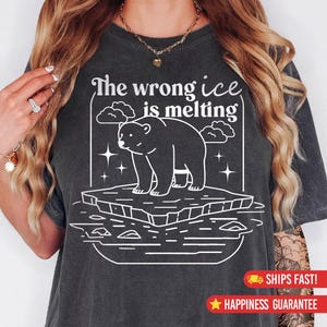 May include: Dark gray t-shirt with a white graphic of a polar bear on a melting iceberg, with the text "The wrong ice is melting". The design includes clouds and stars, promoting an environmental message.