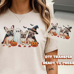 May include: Beige t-shirt featuring a Halloween-themed graphic. The design includes three French Bulldogs, a ghost, pumpkins, and bats. The dogs are dressed in capes and a witch hat. The words "DTF TRANSFER READY TO PRESS" are also visible.