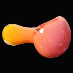 May include: A hand-blown glass pipe with a rounded bowl in shades of pink and a yellow-orange stem. The pipe is designed with a smooth, glossy finish and is set against a black background. This smoking accessory is a unique piece of functional art.