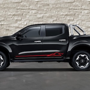 May include: Black pickup truck with red mountain graphic accents. Features include a silver roll bar, black wheels with silver accents, and tinted windows. The truck is parked on a gray surface against a textured brick wall.