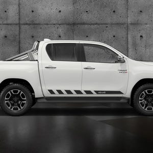 May include: A white pickup truck with black accents, including black wheels and a side stripe. The truck has a roll bar and the text "4x4" on the side. The background is a textured concrete wall.