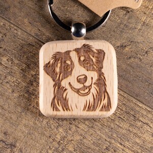 May include: A wooden keychain featuring a laser-etched image of a dog's face. The dog has brown and white markings. The keychain is attached to a metal ring and a brown cardboard tag with the text "T&R Creative Concepts LLC".
