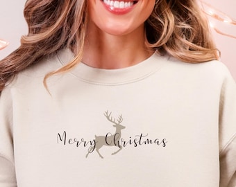 May include: A beige crewneck sweatshirt with the text "Merry Christmas" and a reindeer graphic. The person is wearing light blue jeans and a pair of Christmas-themed slippers. A white mug with a gingerbread man is held in the person's hand.