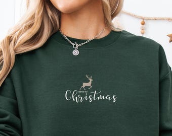 May include: A dark green sweatshirt with the words "Merry Christmas" and a reindeer graphic. The person is wearing red and white plaid pajama pants and holding a mug with a Santa Claus design.