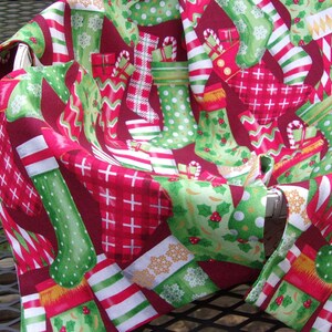 May include: A festive Christmas-themed fabric with a pattern of red, green, and white stockings, gifts, and candy canes. The fabric is draped over an object, showcasing the holiday design. The color palette includes shades of red, green, and white.