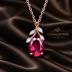 May include: A rose gold necklace featuring a large oval-cut deep pink gemstone pendant accented by three small marquise-cut opals arranged like leaves on a stem. The pendant hangs from a delicate chain and includes the text ANJALIJEWEL.