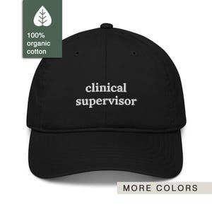 May include: Black baseball cap with the embroidered text "clinical supervisor" in white. The cap is made of 100% organic cotton and has a curved brim. The words "MORE COLORS" are at the bottom.