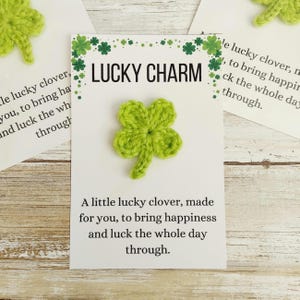 May include: A green crocheted four-leaf clover on a white card with the words "LUCKY CHARM". The card also includes the text: "A little lucky clover, made for you, to bring happiness and luck the whole day through."