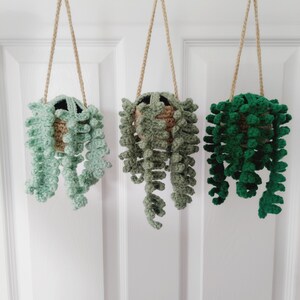 May include: Three crocheted hanging plant pots with green and brown yarn. The pots are suspended from the ceiling by twine.
