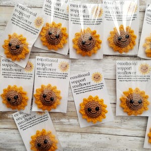 Pu&ograve; includere: Spille a forma di girasole all'uncinetto con facce sorridenti, confezionate su biglietti con testo motivazionale. I girasoli sono gialli con centri marroni e i biglietti hanno una grafica solare. Un articolo fatto a mano.