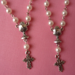 May include: Two white pearl rosaries with silver chalice and cross charms. The chalice charms have the letters "IHS" on them.