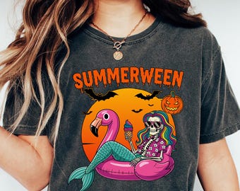 May include: Dark gray t-shirt with the word "SUMMERWEEN" in orange, featuring a skeleton mermaid on a pink flamingo float, holding an ice cream cone. A pumpkin and bats are also in the design.