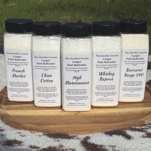 May include: Five clear plastic bottles with black lids, filled with white powder, labeled as carpet dust refreshers. The labels read "French Market", "Clean Cotton", "High Maintenance", "Whiskey Reserve", and "Baccarat Rouge 540".