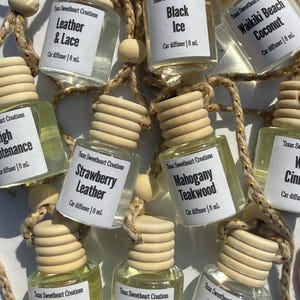 May include: A collection of car air fresheners in small glass bottles with wooden lids and labels. Scents include "Leather & Lace," "Black Ice," and "Waikiki Beach Coconut." Each bottle is 8 mL.